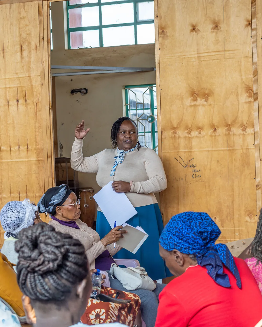 A woman standing with a sheet of notes, speaking to women seated around her