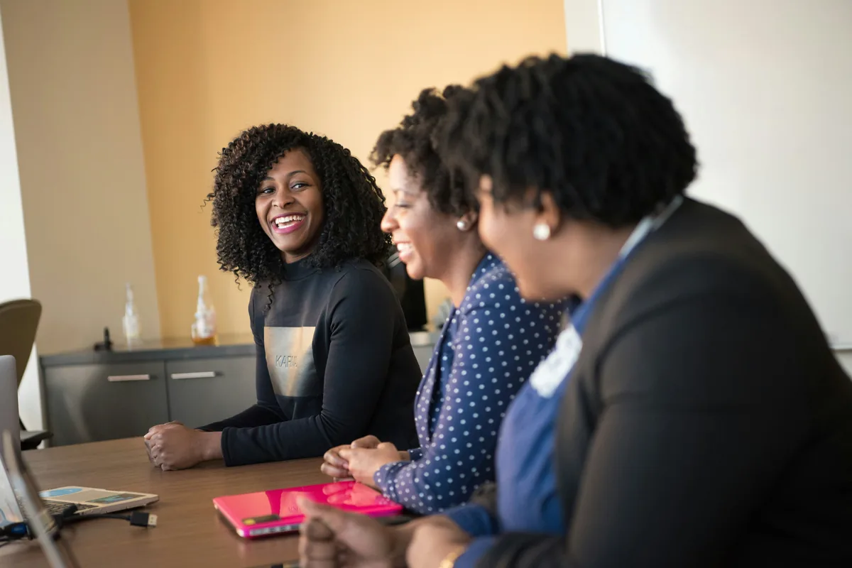 Three women seated around a wooden table in a meeting room, smiling during a discussion